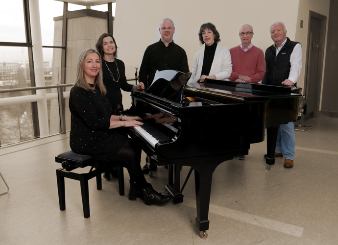 Image of singers standing beside a piano